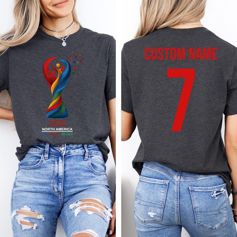 Op de afbeelding: Donkergrijs t-shirt met een kleurrijke afbeelding van een trofee en de tekst "NORTH AMERICA MEXICO". De achterkant van het shirt heeft de tekst "CUSTOM NAME" en het nummer 7 in rood.