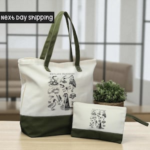 A large white tote bag with a green trim and a smaller white bag with a similar design, both featuring illustrations of various birds and wildlife, are displayed on a wooden surface.