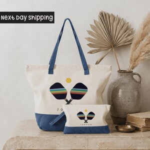 a white tote bag with a blue handle, a smaller bag with a similar design, and a decorative vase with a potted plant on a table.