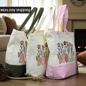 Three colorful tote bags with floral designs and the word "DOULA" printed on them, placed on a wooden surface.