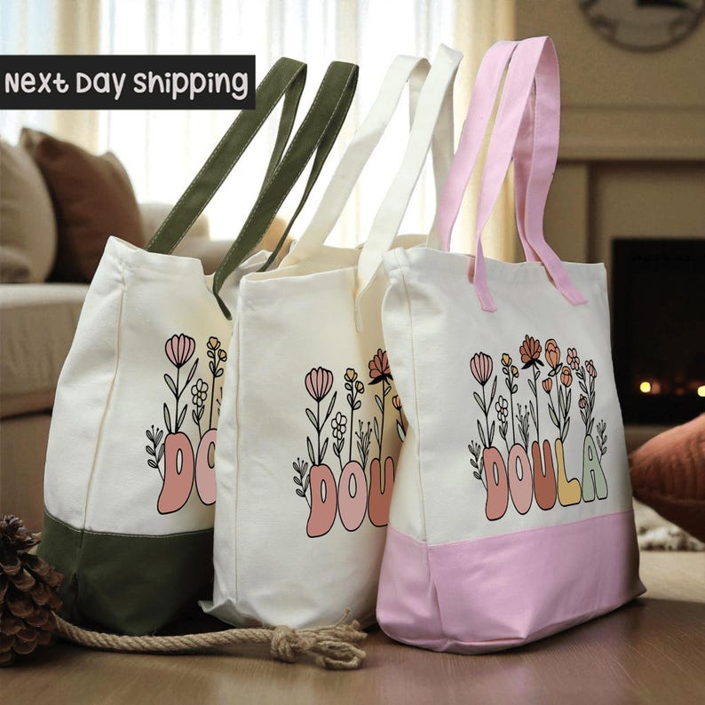 Three colorful tote bags with floral designs and the word "DOULA" printed on them, placed on a wooden surface.