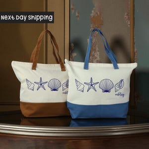 May include: Two canvas tote bags with a beach theme. One has a brown base and handles, the other has a blue base and handles. Both bags are white with blue seashell and starfish designs. The word "ashley" is written on the bottom right of the blue bag.