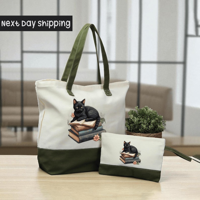 A white tote bag with a green trim and a smaller white bag with a cat design on it, both placed on a wooden surface.