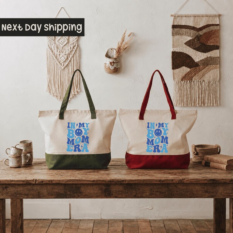 Two tote bags with text printed on them, placed on a wooden table against a wall with a woven wall hanging.