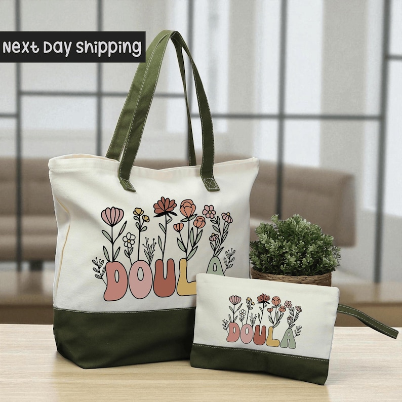 A large white tote bag with a floral design and the word "DOULA" printed on it, along with a smaller white bag or pouch with the same floral design and the word "DOULA" printed on it, placed on a wooden surface.