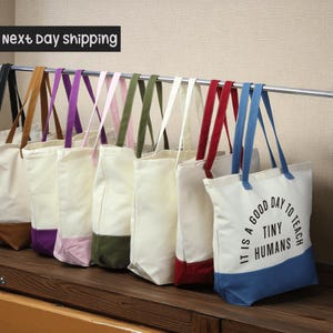 A row of colorful tote bags hanging on a rack, with a sign that says "Next day shipping" above them.