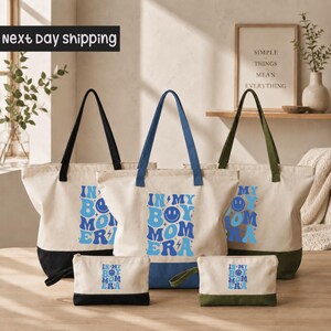 a collection of tote bags and a small bag, all with the same design and text printed on them. The text on the bags reads "IN MY BODY MOMERA".