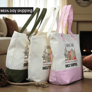 Three tote bags with the text "I HAVE NO SHELF CONTROL" printed on them, placed on a wooden surface.