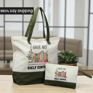 A large white tote bag with a printed design and text, and a smaller white bag with a similar design and text, both placed on a wooden surface.