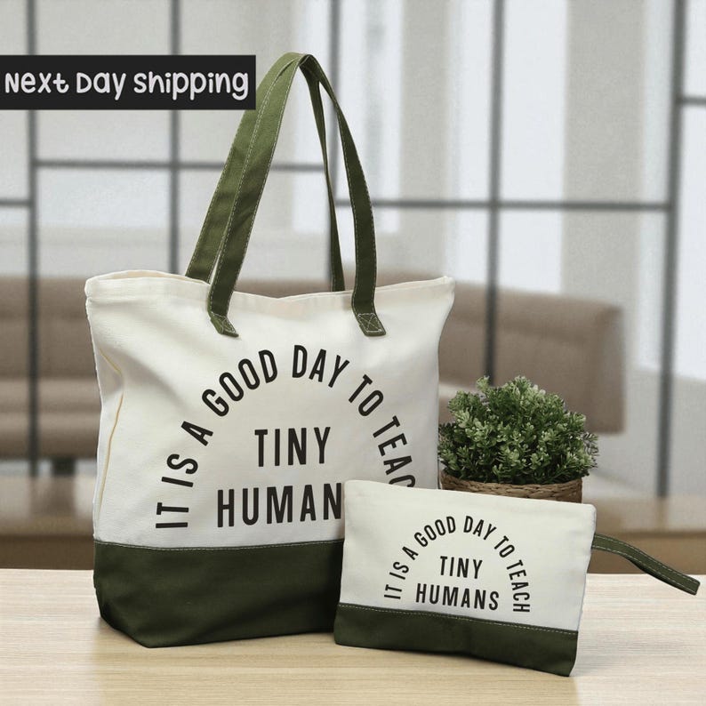 A large white tote bag with a green handle and a smaller white bag with a green handle, both featuring the text "IT IS A GOOD DAY TO TEACH TINY HUMANS" printed on them.