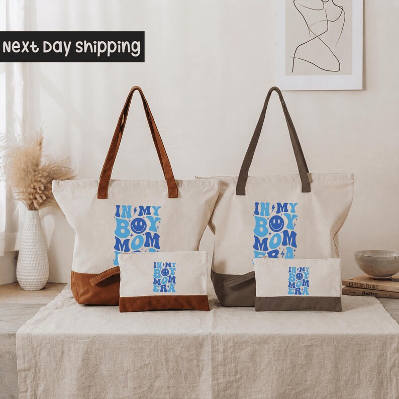 two tote bags with the text "IN MY BOY MOMM" printed on them, along with a small bag and a picture frame on a table.
