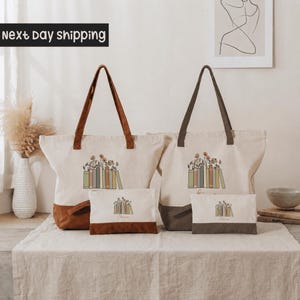 two tote bags with a floral design, placed on a table with a vase and some books.