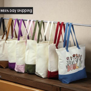 A row of colorful tote bags hanging on a rack, with a sign indicating next day shipping.