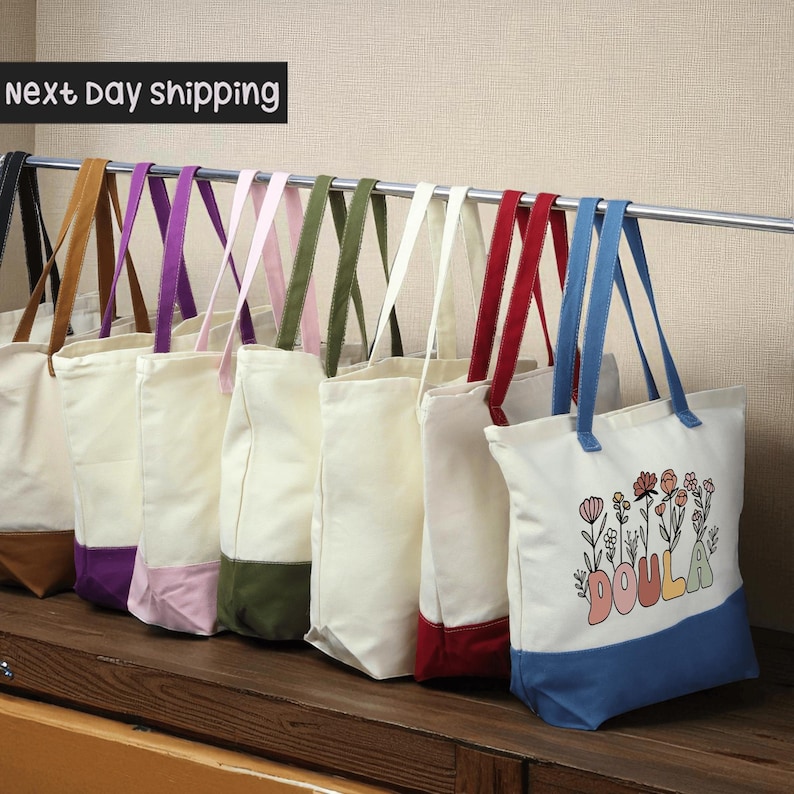 A row of colorful tote bags hanging on a rack, with a sign indicating next day shipping.