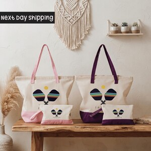 a collection of colorful tote bags and a small bag set, arranged on a wooden surface against a white wall.