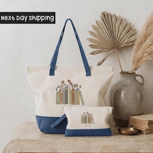 a large tote bag with a book design, a smaller bag, a vase with a potted plant, and some books on a table.