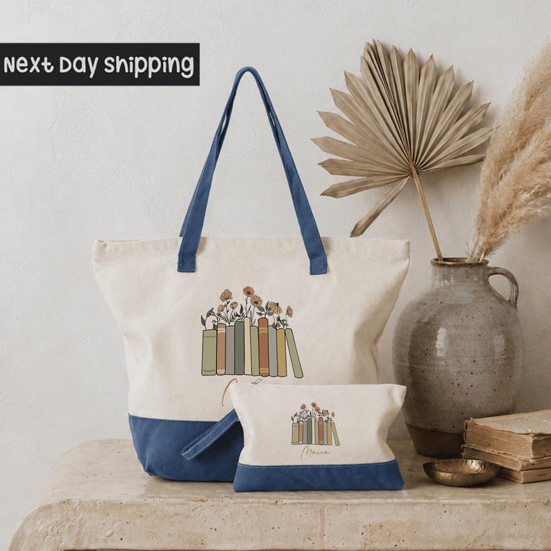 a large tote bag with a book design, a smaller bag, a vase with a potted plant, and some books on a table.