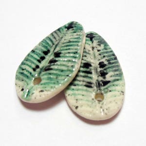 May include: Two ceramic leaf-shaped pendants with a green and black speckled design. The pendants have a hole in the center for stringing.