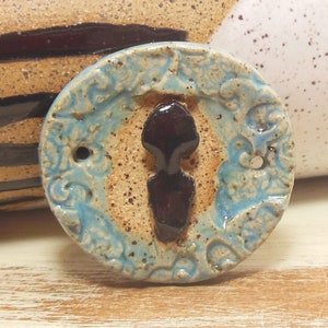 May include: A round ceramic tile with a blue and brown glaze. The tile features a raised design of a keyhole with a brown key.
