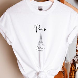 May include: White t-shirt featuring a black graphic of the Eiffel Tower with the word "Paris" above and "Je t'aime FRANCE" below. The shirt is knotted at the waist.