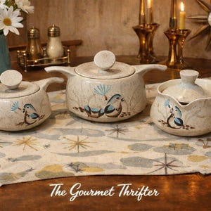 Könnte beinhalten: Ein Set aus drei Vintage-Servierschalen aus Keramik mit Deckeln und Griffen. Die Schalen sind beige gesprenkelt mit einem blauen Vogeldesign. Das Logo The Gourmet Thrifter ist sichtbar.