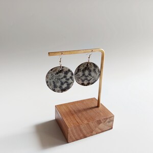 Peut inclure: Une paire de boucles d'oreilles rondes en argent avec un motif noir et blanc. Les boucles d'oreilles sont présentées sur un support en bois.