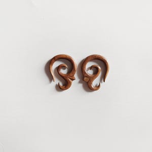 May include: A pair of wooden ear gauges with a unique, intricate design. The gauges are brown and have a swirling pattern.