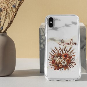 May include: A clear phone case with a fall-themed design featuring a pumpkin, leaves, and wheat. The name "Amelia" is printed on the case.