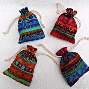 May include: Four small fabric drawstring pouches featuring vibrant, multi-colored patterns. Each bag has a cream-colored cord closure. The designs include horizontal stripes, geometric shapes, and intricate swirls in shades of blue, red, orange, and green.