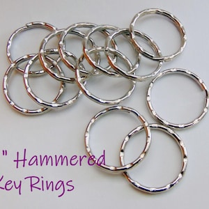 May include: A collection of silver-colored, hammered key rings. The rings are approximately 1 inch in diameter and have a textured surface. The text "1" Hammered Key Rings" is displayed in purple.