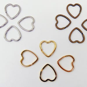 May include: An assortment of heart-shaped metal clasps in silver, gold, and bronze tones. The clasps are arranged in clusters of four and five, showcasing their different finishes and designs. Ideal for jewelry making.