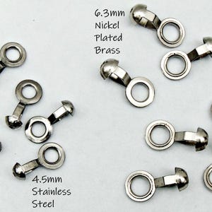 May include: Close-up of several small, silver-colored metal fasteners. The image includes text that reads "6.3mm Nickel Plated Brass" and "4.5mm Stainless Steel". The fasteners have a rounded head and a circular loop.