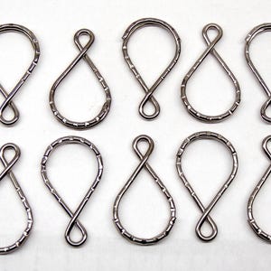 May include: Ten silver-toned metal split rings arranged in two rows. Each ring features a twisted, teardrop-shaped design with a textured, notched outer edge. The metal has a smooth, reflective finish, and the rings are uniform in size and shape.