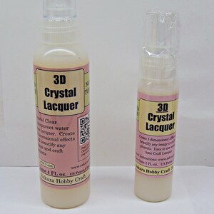 May include: Two bottles of 3D Crystal Lacquer. The bottles have a clear plastic cap and a pink and cream label with the product name and details. The larger bottle contains 4 fl oz of lacquer, and the smaller bottle contains 2 fl oz.