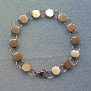 May include: A silver-toned metal bracelet composed of a series of circular, flat discs connected by small, thin jump rings. The bracelet features a lobster claw clasp mechanism at the bottom, securing the circular chain into a continuous loop.