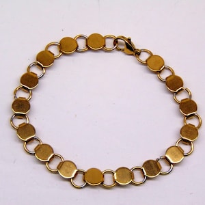 May include: A gold-toned bracelet constructed from a series of circular metal discs linked together by small, thin jump rings. The bracelet features a lobster claw clasp mechanism at one end to secure the circular chain design.