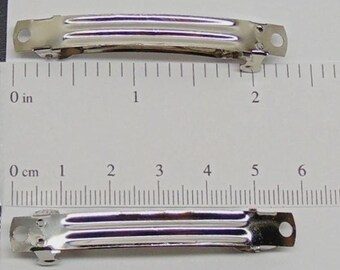 May include: Two silver-colored metal hair barrettes. Each barrette is approximately 2 inches long. The barrettes have a simple, functional design with a series of parallel ridges and a spring-loaded clasp. The barrettes are shown against a white background with a ruler.