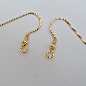 May include: Two gold-colored earring hooks. Each hook has a curved wire for the ear, a coiled spring, a small round bead, and a loop at the bottom for attaching charms or other decorative elements. The hooks are designed for jewelry making.