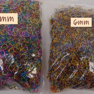 May include: Two clear plastic bags filled with small metal jump rings. The left bag contains multicolored rings labeled 8mm, while the right bag contains gold and bronze-toned rings labeled 6mm. These circular metal components are used for jewelry making.