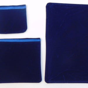 May include: Three navy blue velvet pouches with blue zippers. The pouches are in different sizes: a small square, a medium rectangle, and a large rectangle. The velvet has a soft, luxurious appearance.