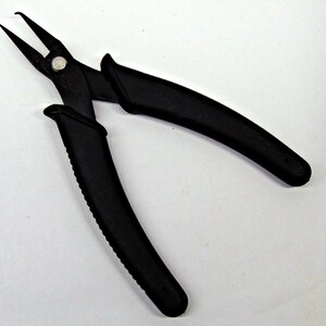 May include: Black needle-nose pliers with a silver rivet. The pliers have a curved handle with a textured grip for secure handling. The tool's jaws are pointed and designed for precision work.