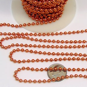 May include: Copper-colored ball chain, shown in a close-up view. The chain is coiled on a white spool and also laid out in several strands. A US quarter is included for size comparison. The chain is made of small, round beads.