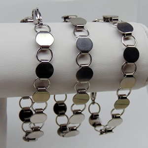 May include: Three silver-toned bracelets with a chain of connected, flat, oval and circular links. The bracelets are displayed on a white surface. The bracelets have a clasp closure.