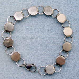 May include: A silver-toned bracelet featuring a series of flat, circular links connected by small, round rings. The bracelet has a secure clasp. The jewelry is displayed against a light blue background.