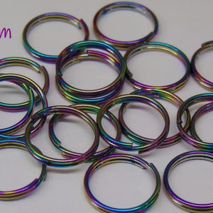 May include: A collection of circular metal split rings with an iridescent rainbow finish. Each ring features a double-loop design and measures 12mm in diameter. The metallic surface reflects various colors including blue, purple, and green tones.