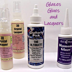May include: Four bottles of craft supplies, including 3D Crystal Lacquer and Diamond Glaze. The bottles are white with colorful labels and white caps. The text "Glazes, Glues and Lacquers" is written in purple.
