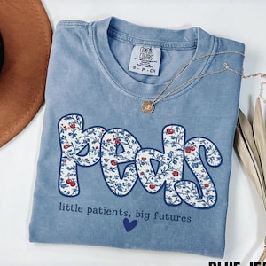 blue Jean Comfort Colors pediatric nurse shirt with floral “Peds” typography and quote “little patients, big futures,” trendy coquette style RN gift tee.