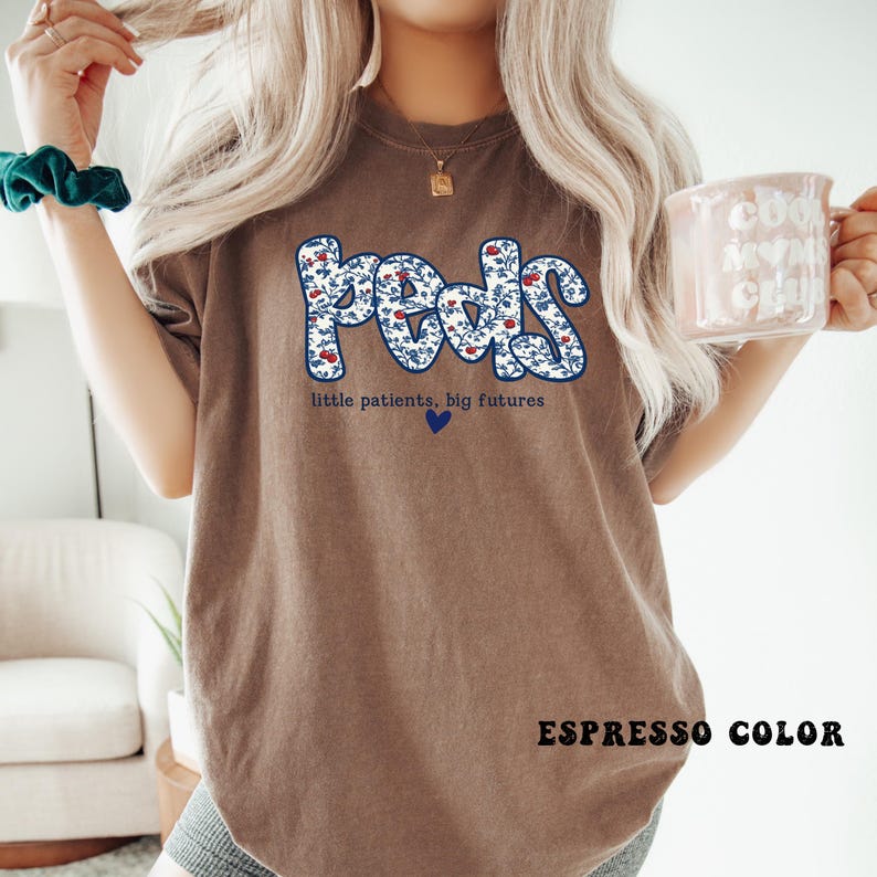 K&ouml;nnte beinhalten: Espressofarbenes T-Shirt mit dem Wort "Peds" in einem floralen Design. Der Text "little patients, big futures" und ein blaues Herz befinden sich unter dem Wort "Peds". Die Worte "ESPRESSO COLOR" stehen am unteren Rand des T-Shirts.