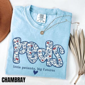 Light blue Comfort Colors pediatric nurse shirt with floral “Peds” typography and quote “little patients, big futures,” trendy coquette style RN gift tee.