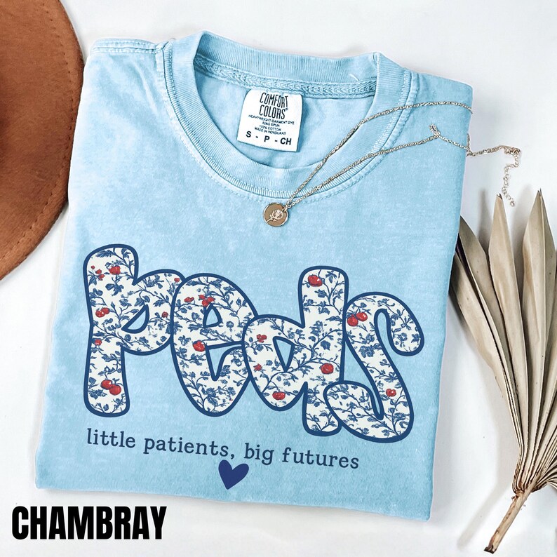 Light blue Comfort Colors pediatric nurse shirt with floral “Peds” typography and quote “little patients, big futures,” trendy coquette style RN gift tee.